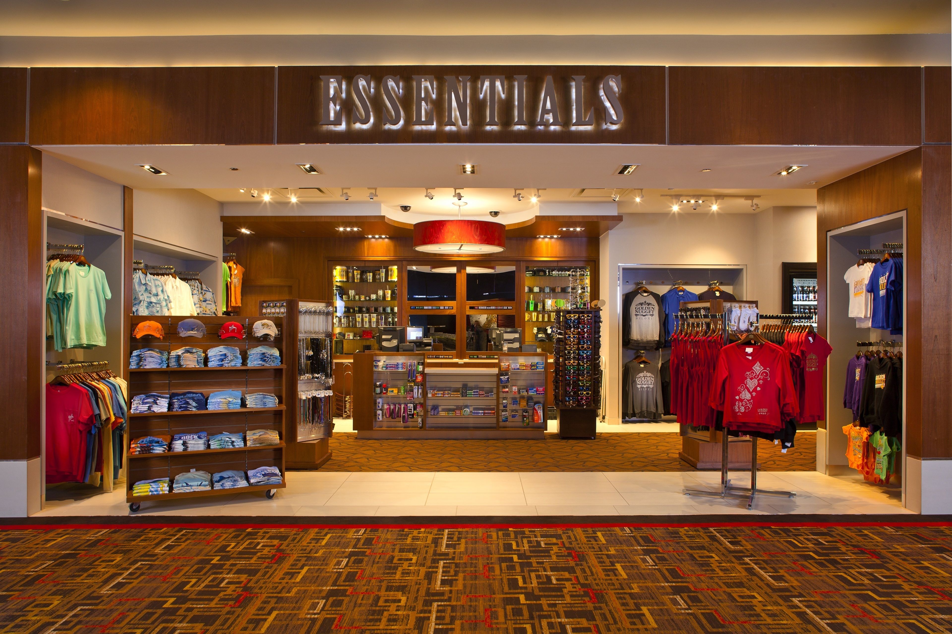 Una tienda llamada 'ESSENTIALS' con estantes llenos de ropa y accesorios, una caja registradora y una exhibición de sombreros.