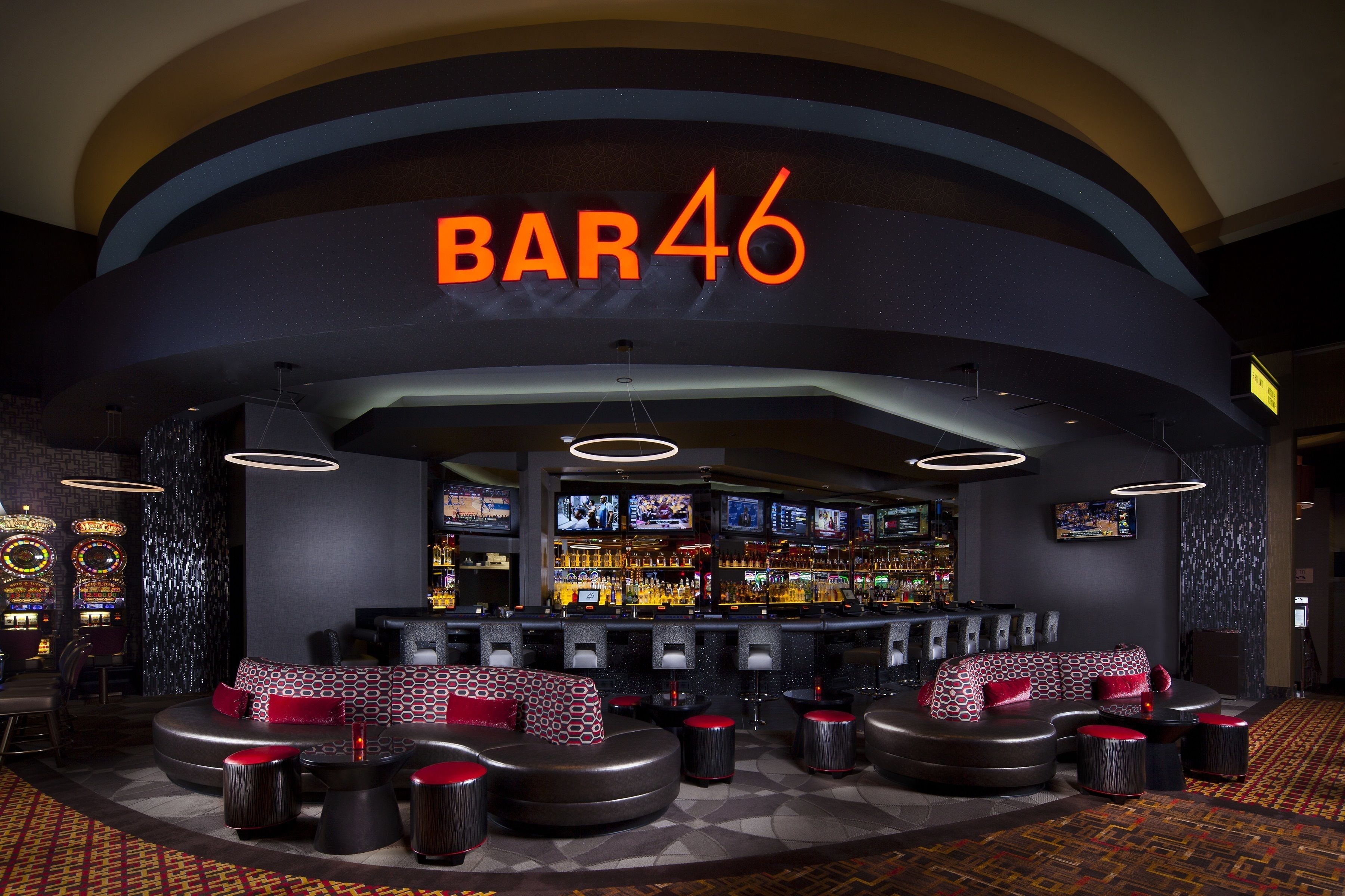 Un bar llamado BAR46 con un diseño moderno, que presenta una zona de asientos curva con cojines estampados y una barra bien surtida.