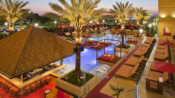 A resort pool area with lounge chairs, palm trees, and a bar.