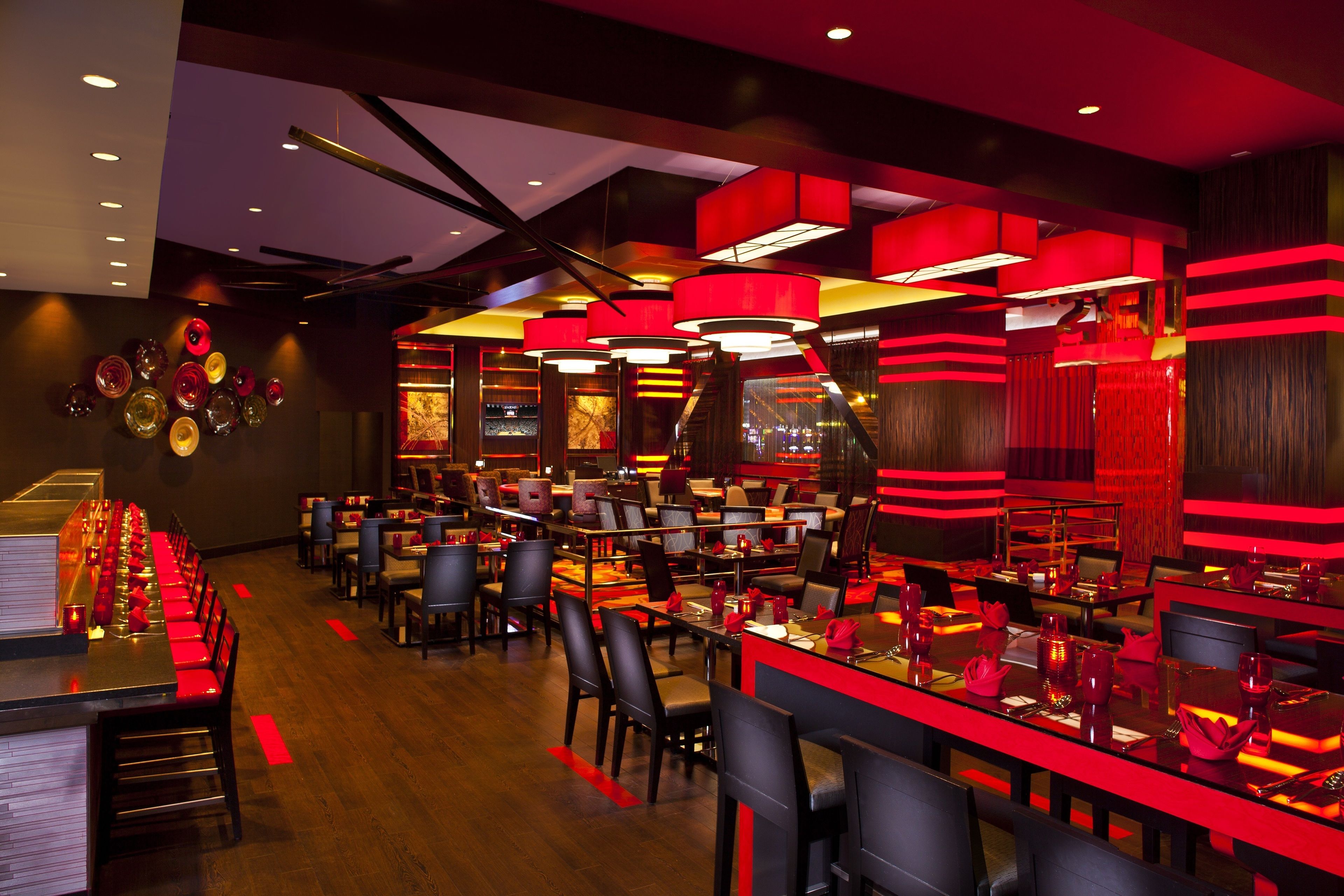 A restaurant with multiple dining tables and chairs, red and black decor, and a modern ceiling design.