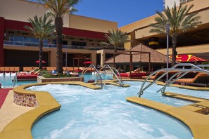 Relax by the resort pool surrounded by lounge chairs and umbrellas, with a clear water feature and stunning views of the surrounding buildings.
