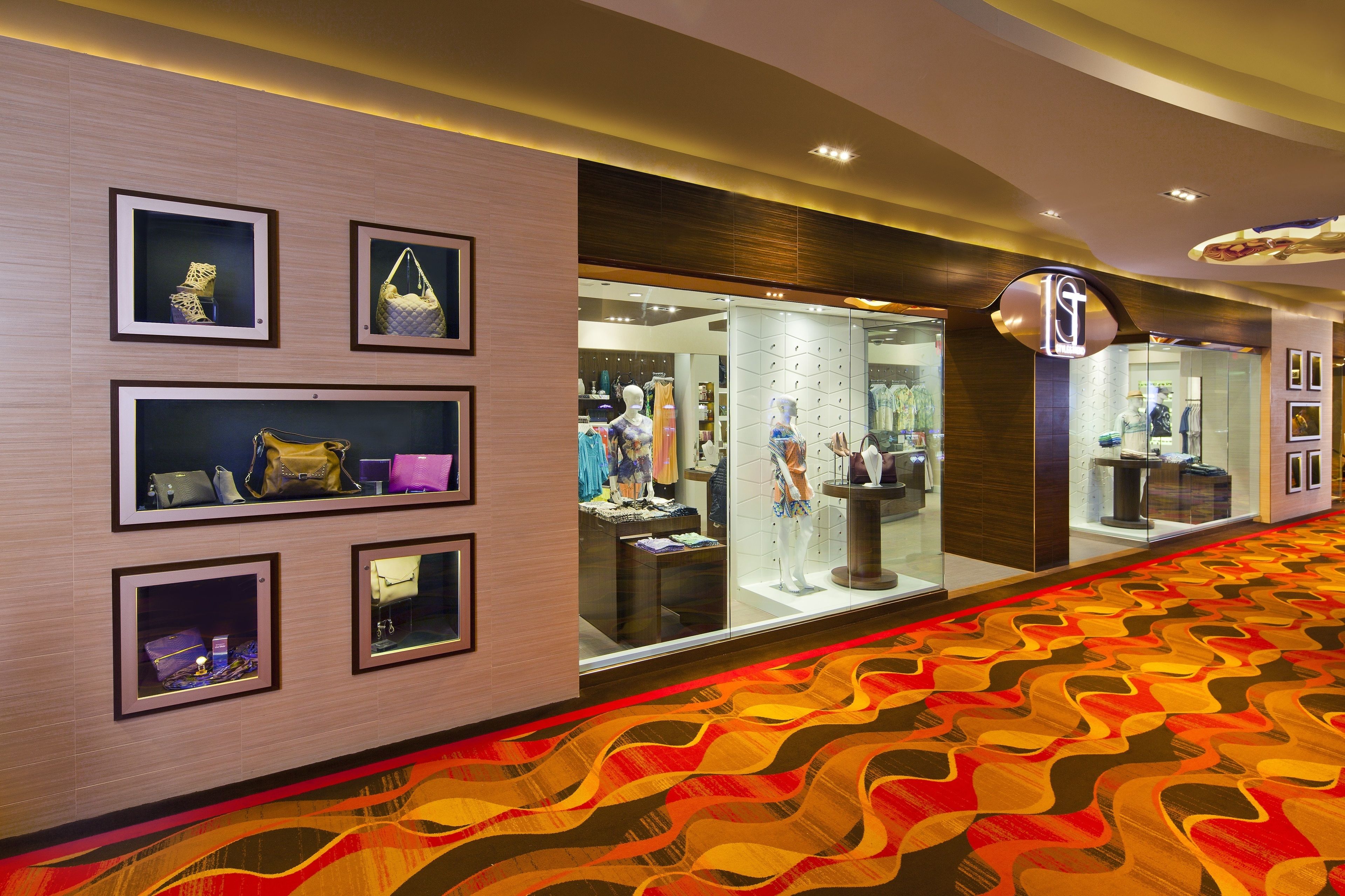 A hotel corridor with framed handbags on display, a patterned carpet, and a visible store with clothing and accessories.