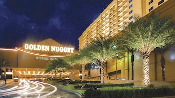 The exterior of the Golden Nugget Hotel & Casino with a night sky, palm trees, and a curved road with light trails.
