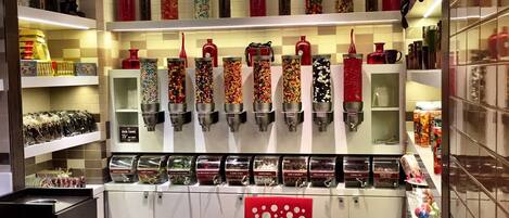 Una tienda de dulces con estantes llenos de caramelos de colores y una zona de estar con sillas rojas.