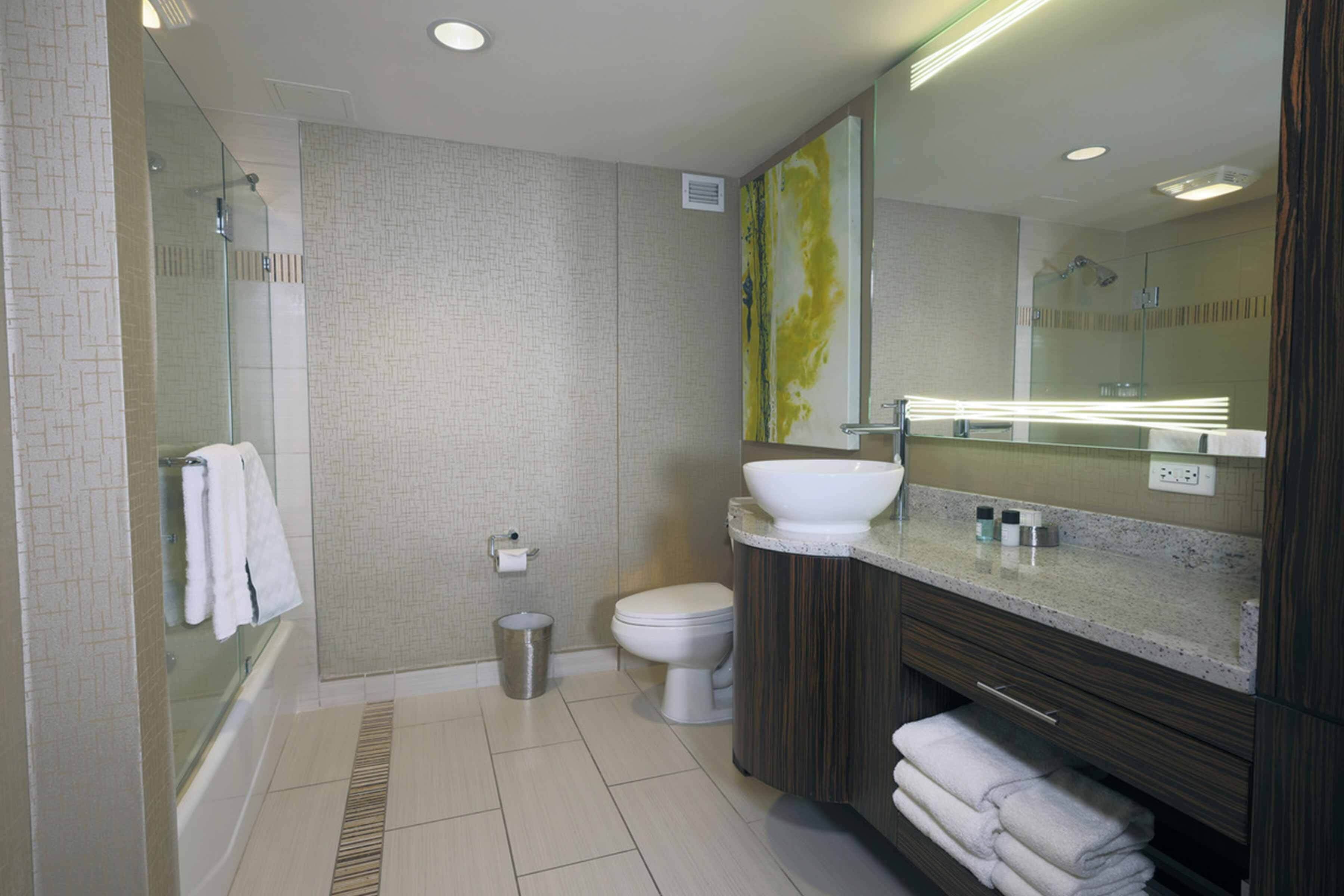 A modern bathroom with a glass-enclosed shower, a white toilet, a large mirror, and a vanity with a sink and towel rack.