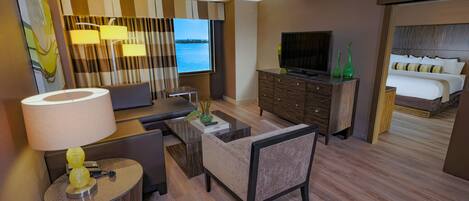 Een hotelkamer met een bank, salontafel, televisie, bed en uitzicht op het water.