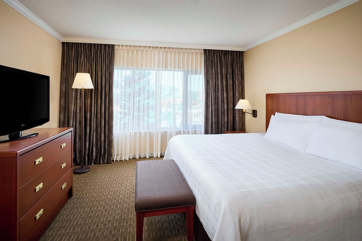 A hotel room with a bed, a TV on a wooden dresser, a bench, and two lamps.