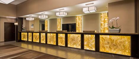 A reception area with a marble counter, overhead lighting, and a potted orchid.