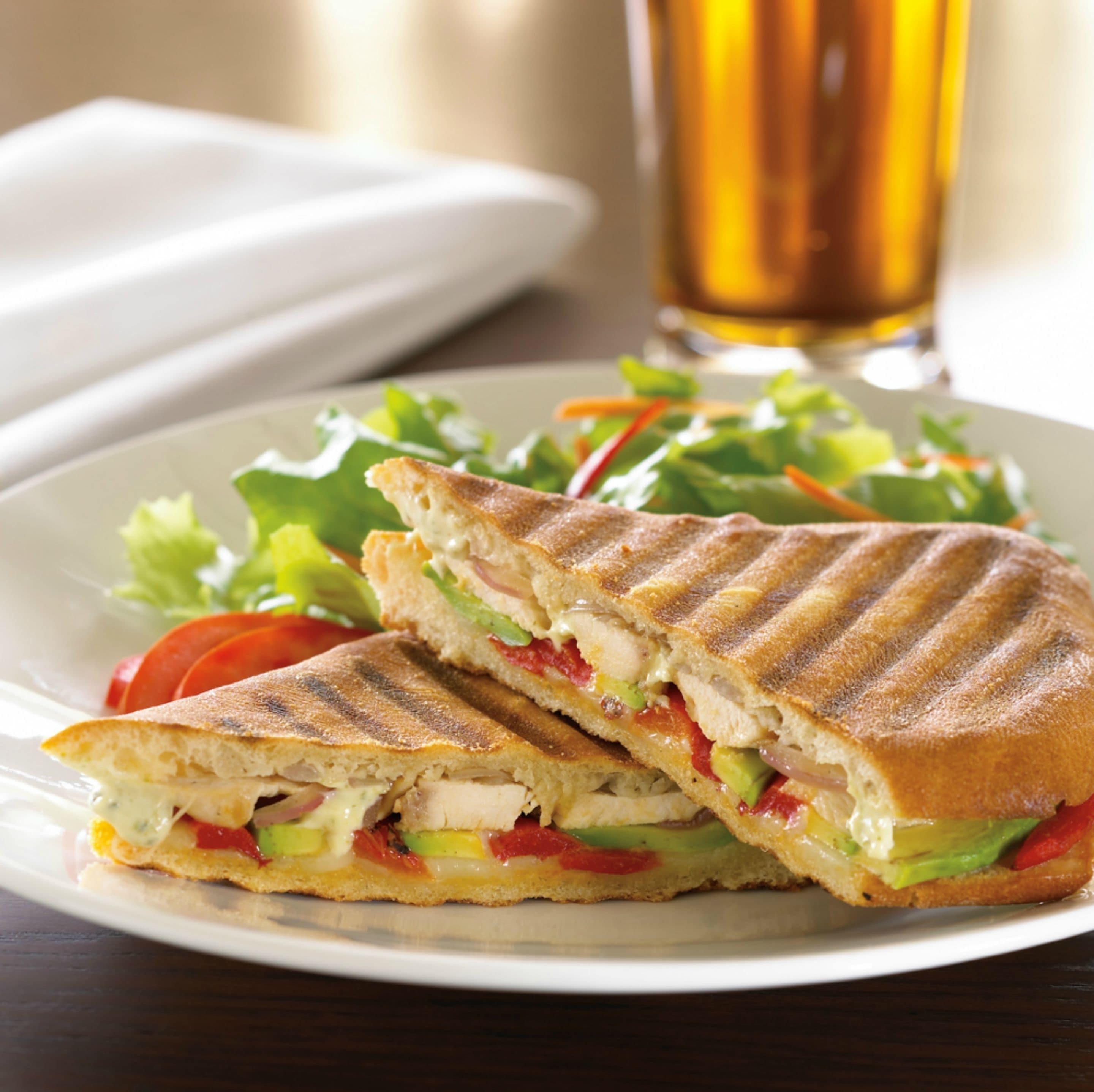 A sandwich cut in half on a plate, with a glass of beer in the background.