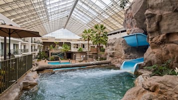 Experience the soothing sound of a cascading waterfall in a serene, naturally lit space surrounded by lush greenery and rocky outcroppings.