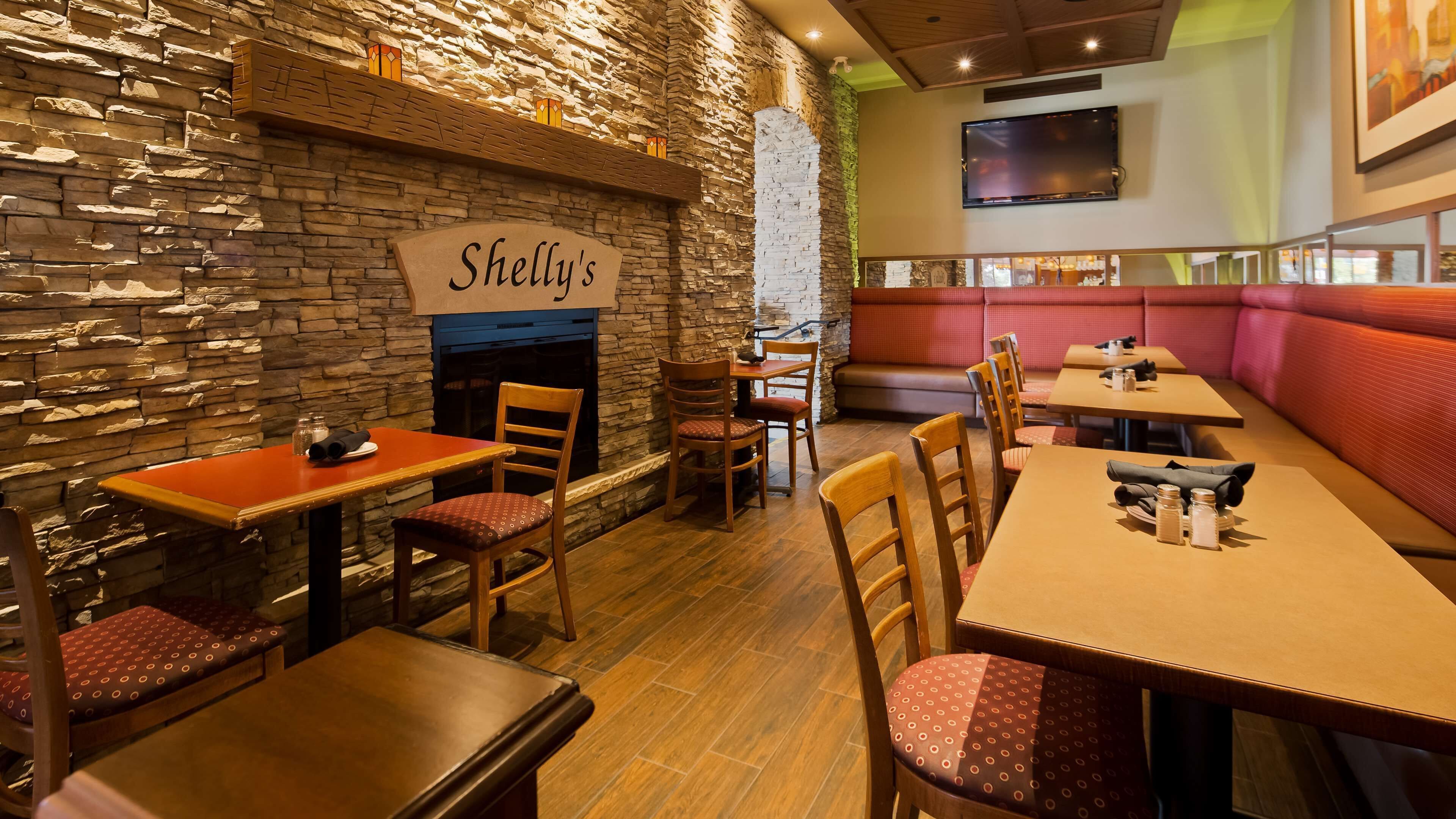 Ein Restaurant mit Stehwänden, Holztischen und -stühlen, einem Kamin und einem an der Wand befestigten Fernseher.