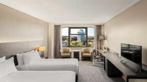 A hotel room with two beds, a desk, a TV, and a view of a cityscape. - The Sydney Boulevard Hotel by Accor (Woolloomooloo)