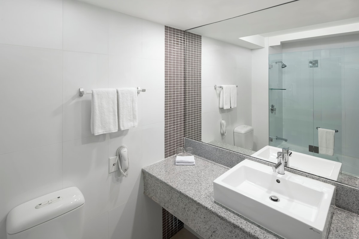A modern bathroom with a large mirror, two sinks, and a toilet.