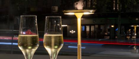 Two glasses of champagne on a table with a gold lamp, a bowl of snacks, and a view of a city street at night.