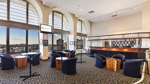 A hotel bar with a city view, featuring tables and chairs, a bar counter, and a large screen. - The Sydney Boulevard Hotel by Accor (Woolloomooloo)