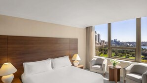 A hotel room with a large bed, two bedside tables with lamps, a chair, and a view of a cityscape. - The Sydney Boulevard Hotel by Accor (Woolloomooloo)