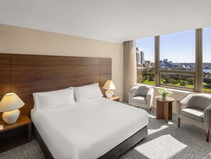 Una camera d'albergo con un letto grande, due comodini con lampade, una sedia e vista sulla città.