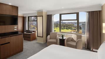 A hotel room with a bed, a desk, a TV, and a view of the city.
