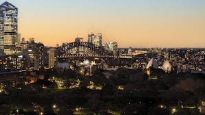 A cityscape at dusk with a prominent bridge and modern buildings. - The Sydney Boulevard Hotel by Accor (Woolloomooloo)