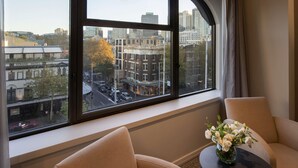 A room with a large window overlooking a cityscape, a sofa, and a small table with a vase of flowers. - The Sydney Boulevard Hotel by Accor (Woolloomooloo)