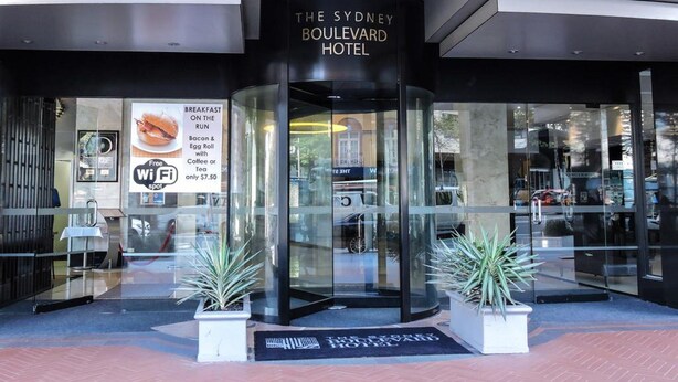 The Sydney Boulevard Hotel entrance with a glass facade, a signboard advertising breakfast, and potted plants. - The Sydney Boulevard Hotel by Accor (Woolloomooloo)
