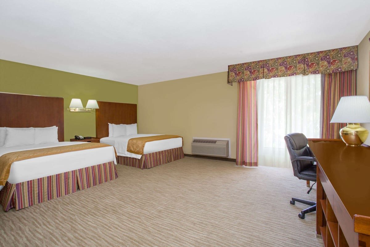 A hotel room with two beds, a desk, a chair, a lamp, and a window with curtains.