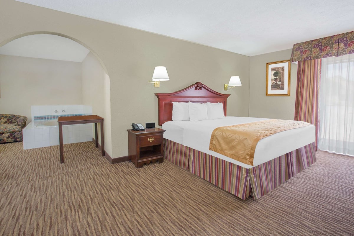 A hotel room with a large bed, a nightstand, a desk, and a chair.