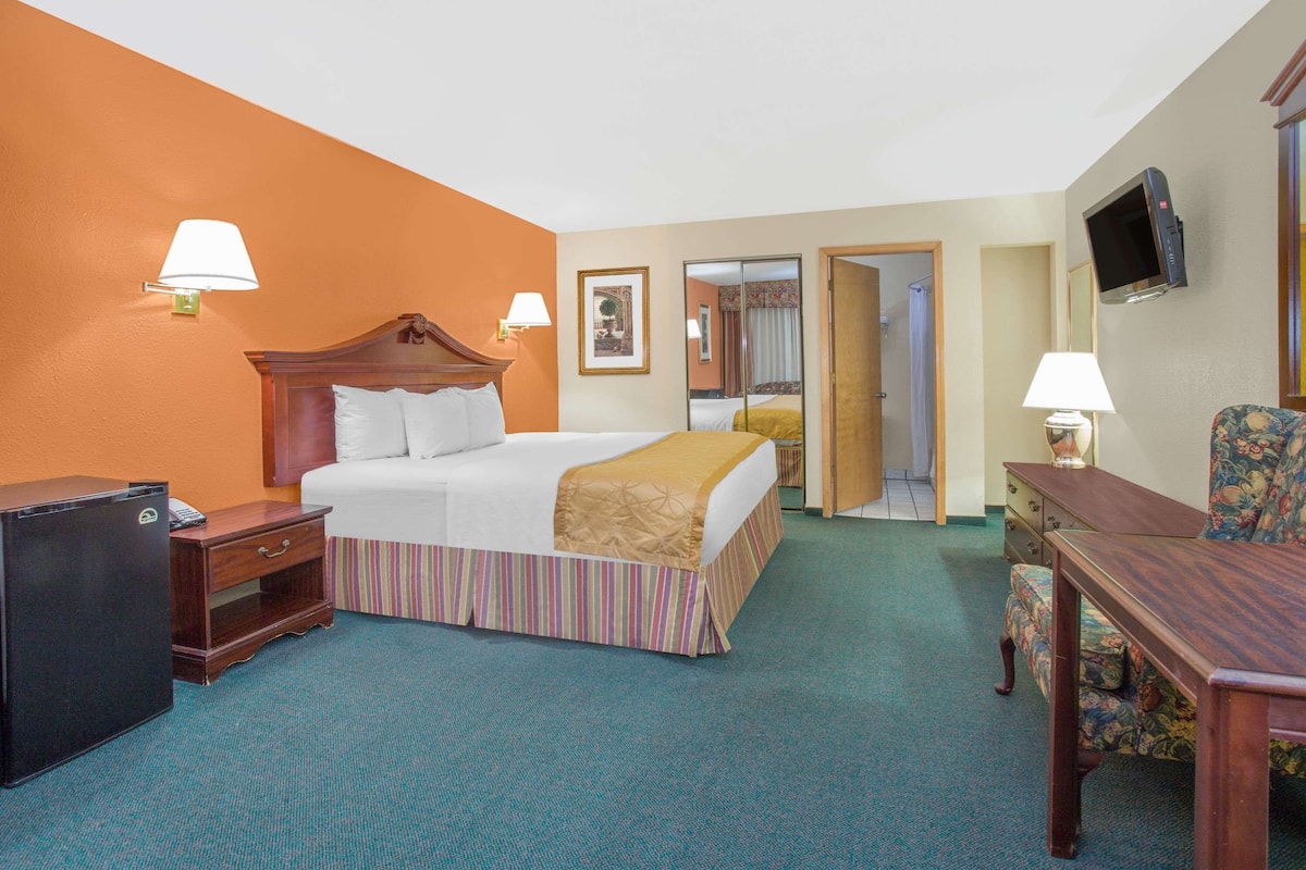 A hotel room with a bed, bedside table, lamp, TV, and a small desk with a chair.