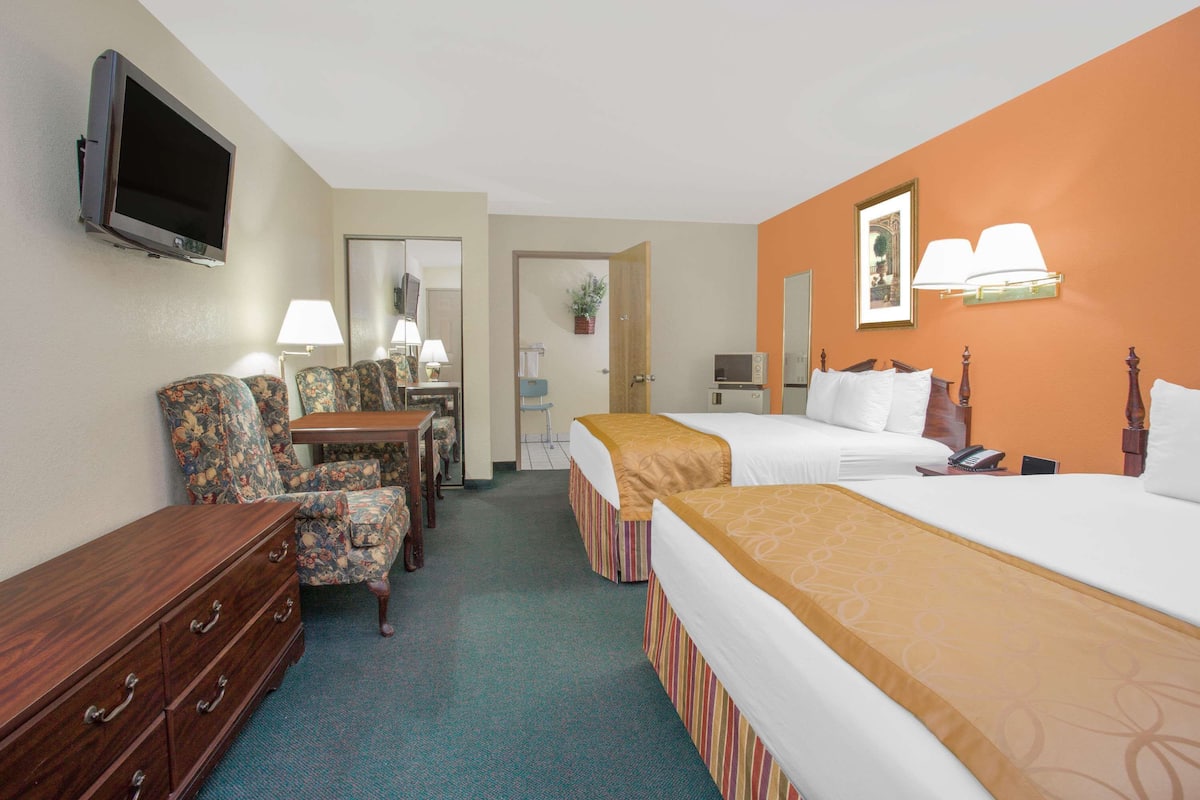 A hotel room with two beds, a TV, a desk with a chair, and a dresser.