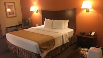 Une chambre d’hôtel avec un grand lit, deux lampes de chevet, une table de chevet avec un téléphone et une horloge, et un tableau encadré au mur.