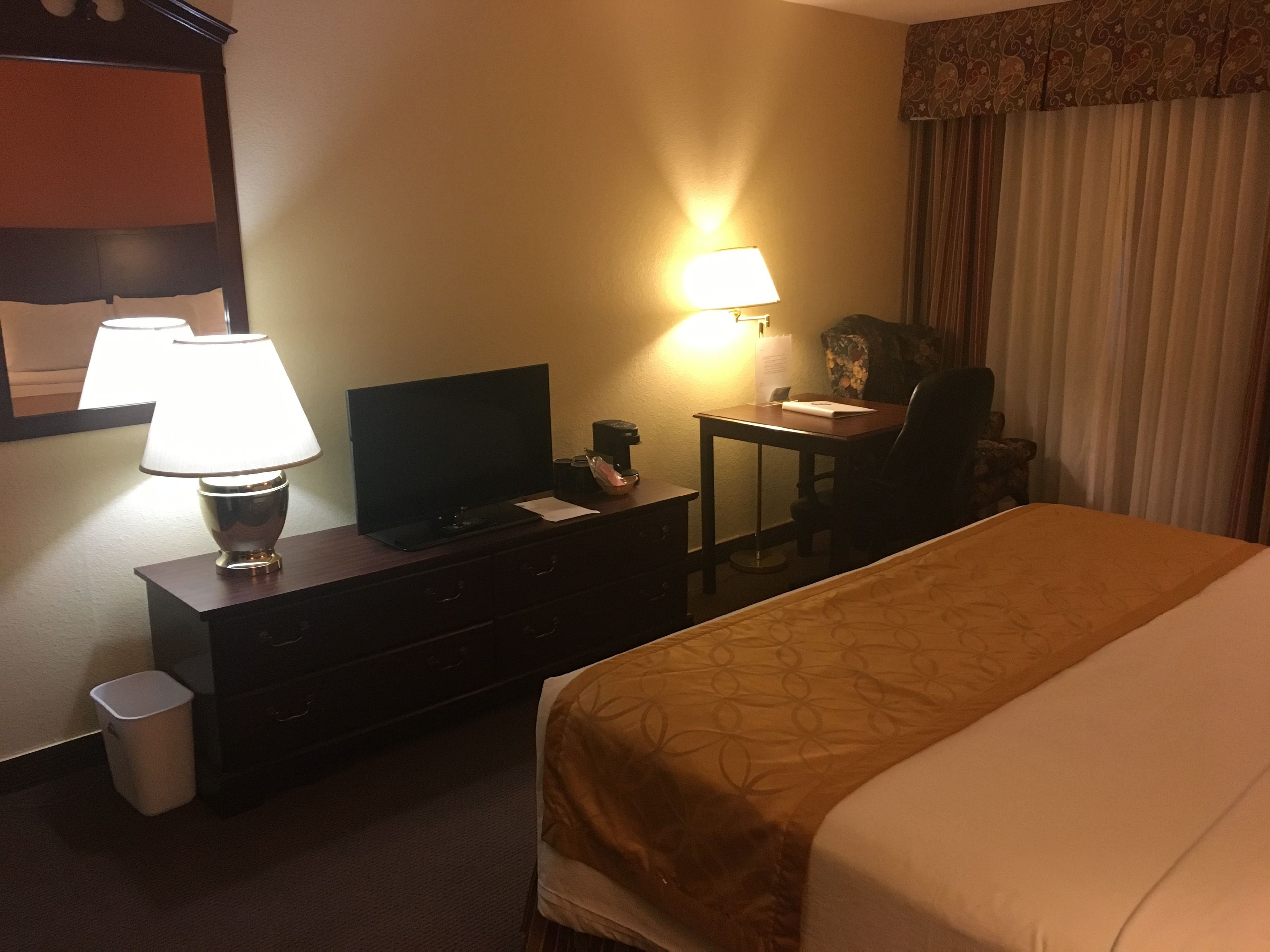 Une chambre d’hôtel avec un lit, un bureau avec une lampe, une télévision et une poubelle.