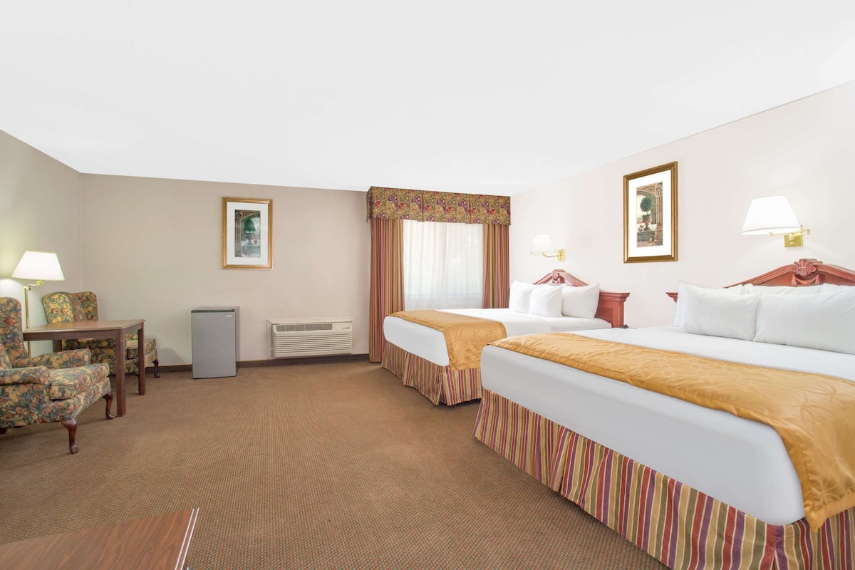 A hotel room with two beds, a desk, a chair, a small table, and a heater.