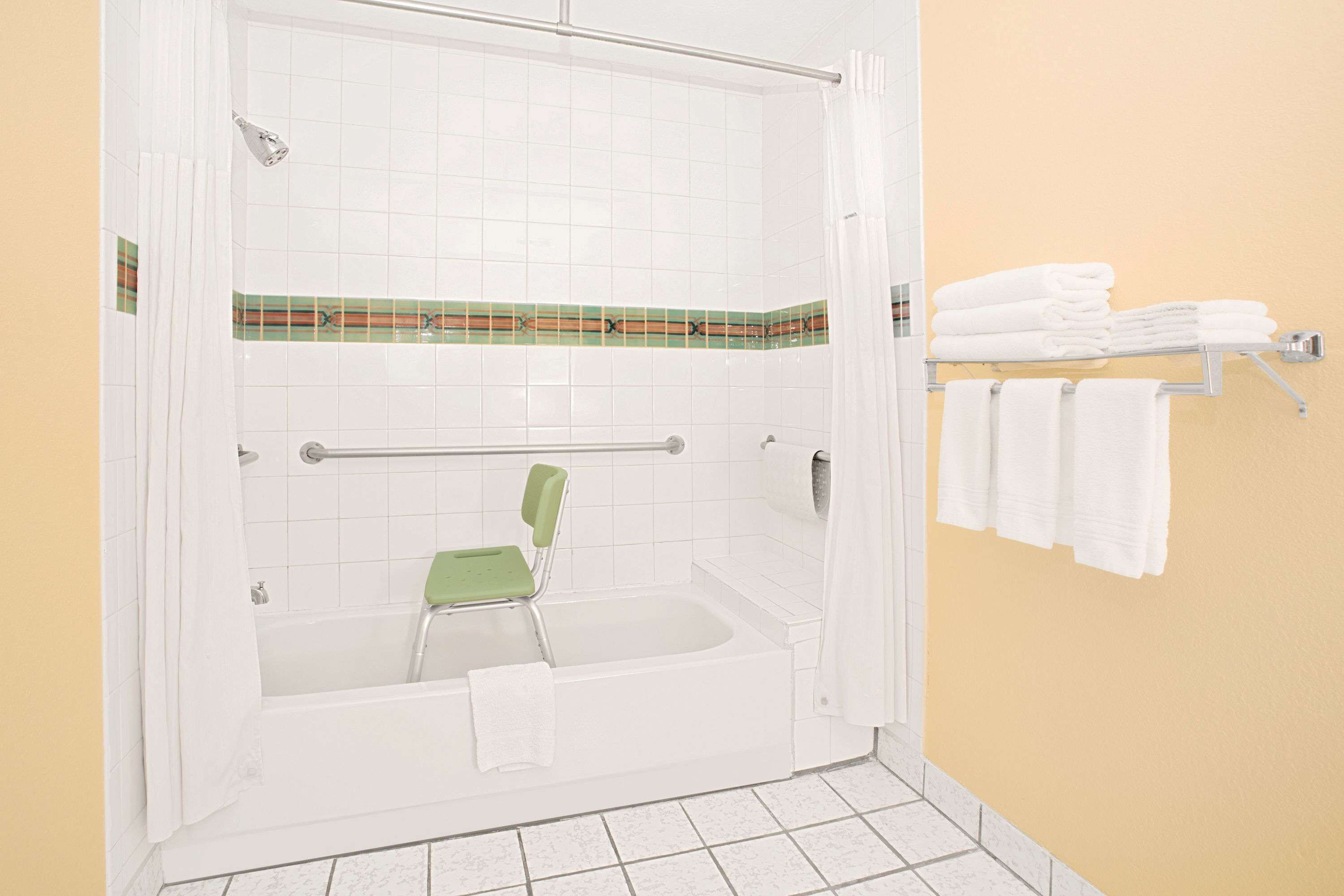 Une douche à l’italienne avec une chaise verte, des carreaux blancs et un porte-serviettes où sont pliées des serviettes.