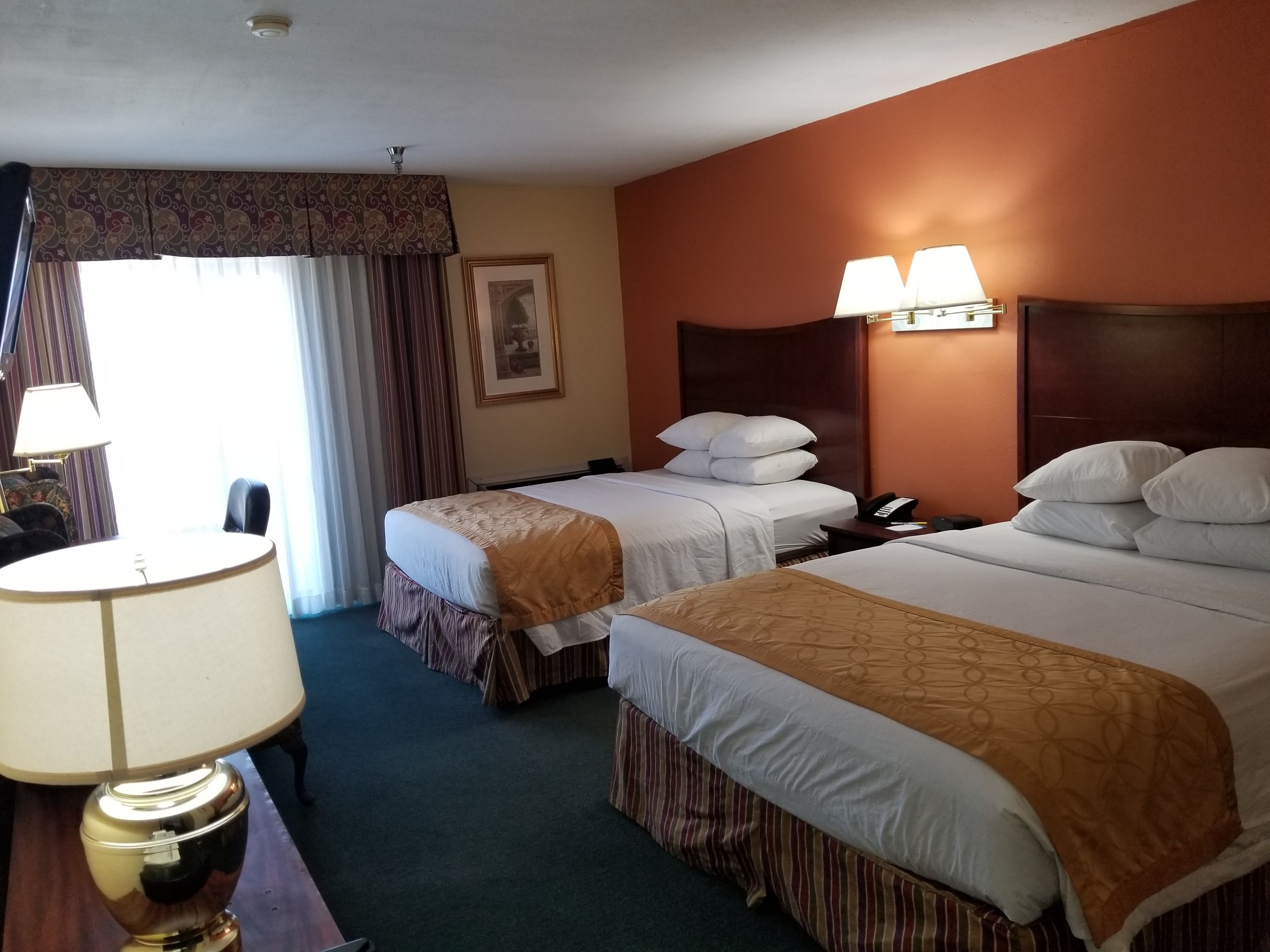 Quarto de hotel com duas camas, uma escrivaninha com abajur, telefone e um quadro na parede.