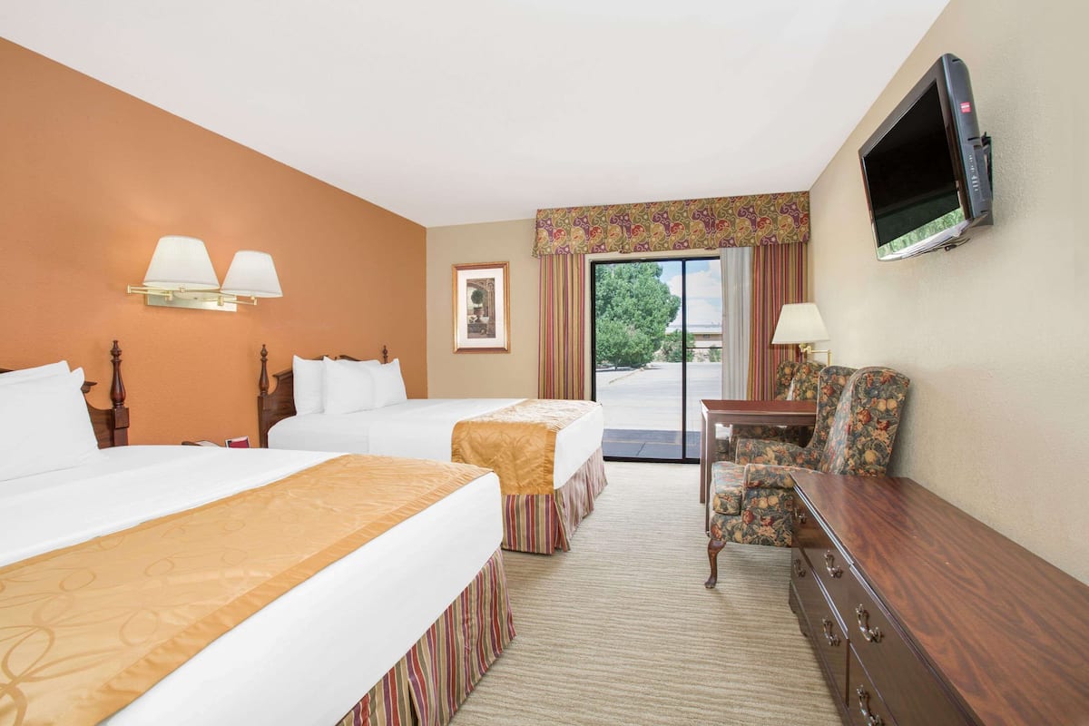 A hotel room with two beds, a television, a desk with a chair, and a view of the outdoors.