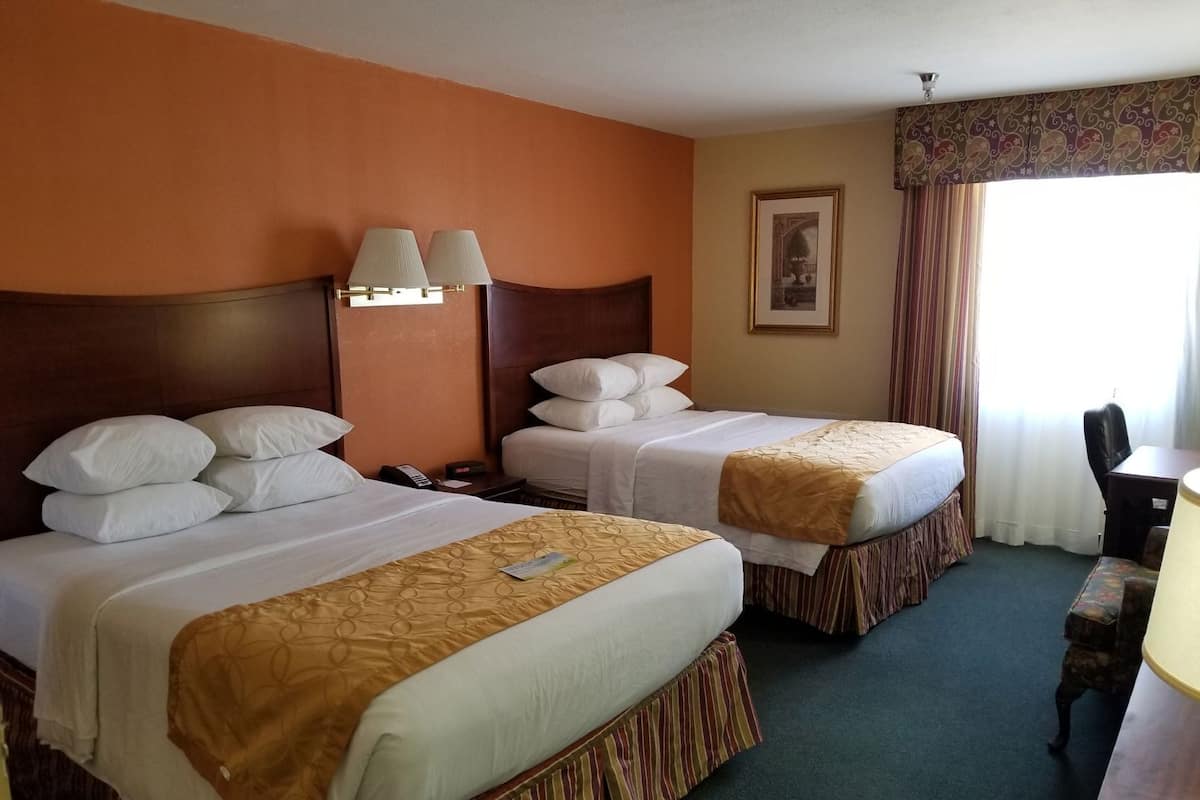 A hotel room with two beds, a desk, a chair, and a window with curtains.