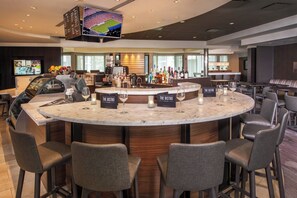A modern bar area with a marble counter, multiple seating options, and a television mounted on the ceiling.