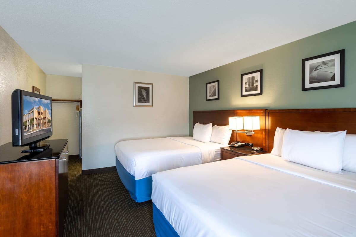 A hotel room with two beds, a desk with a television, and framed pictures on the wall.