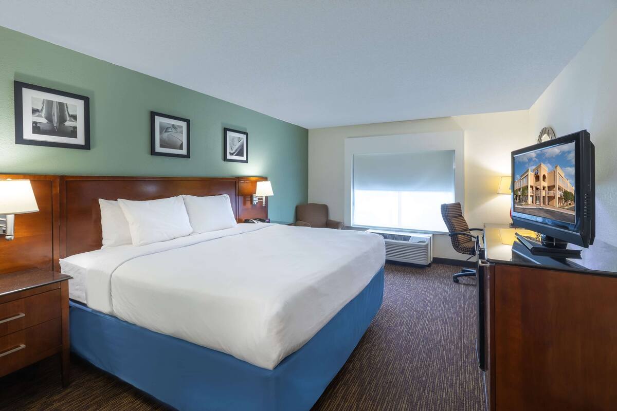 A hotel room with a large bed, a desk with a television, a chair, and framed pictures on the wall.