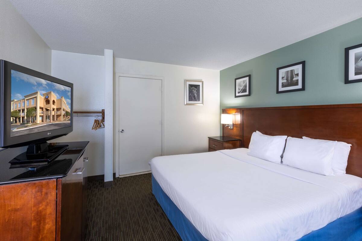 A hotel room with a bed, a TV on a stand, a nightstand with a lamp, and framed pictures on the wall.