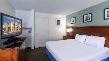 A hotel room with a bed, a TV on a stand, a nightstand with a lamp, and framed pictures on the wall.