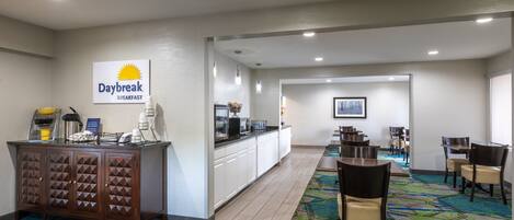A hotel breakfast area with a sign reading "Daybreak Breakfast," a counter with kitchen appliances, and a carpeted floor.