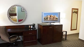 A hotel room with a desk, chair, television, and a mirror.