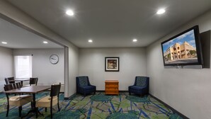 A conference room with a table and chairs, a clock, a framed picture, and a television displaying a building. - Days Inn by Wyndham Greenville (Greenville)