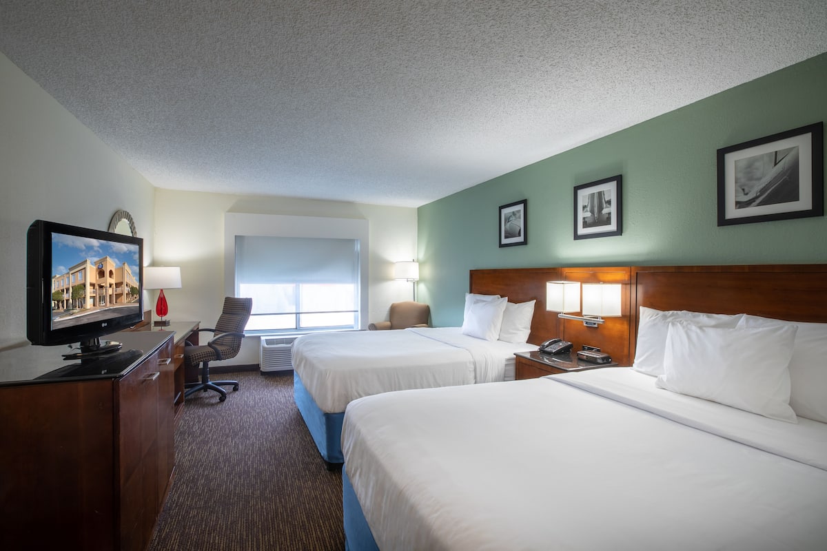 A hotel room with two beds, a desk with a computer, a chair, and a window.