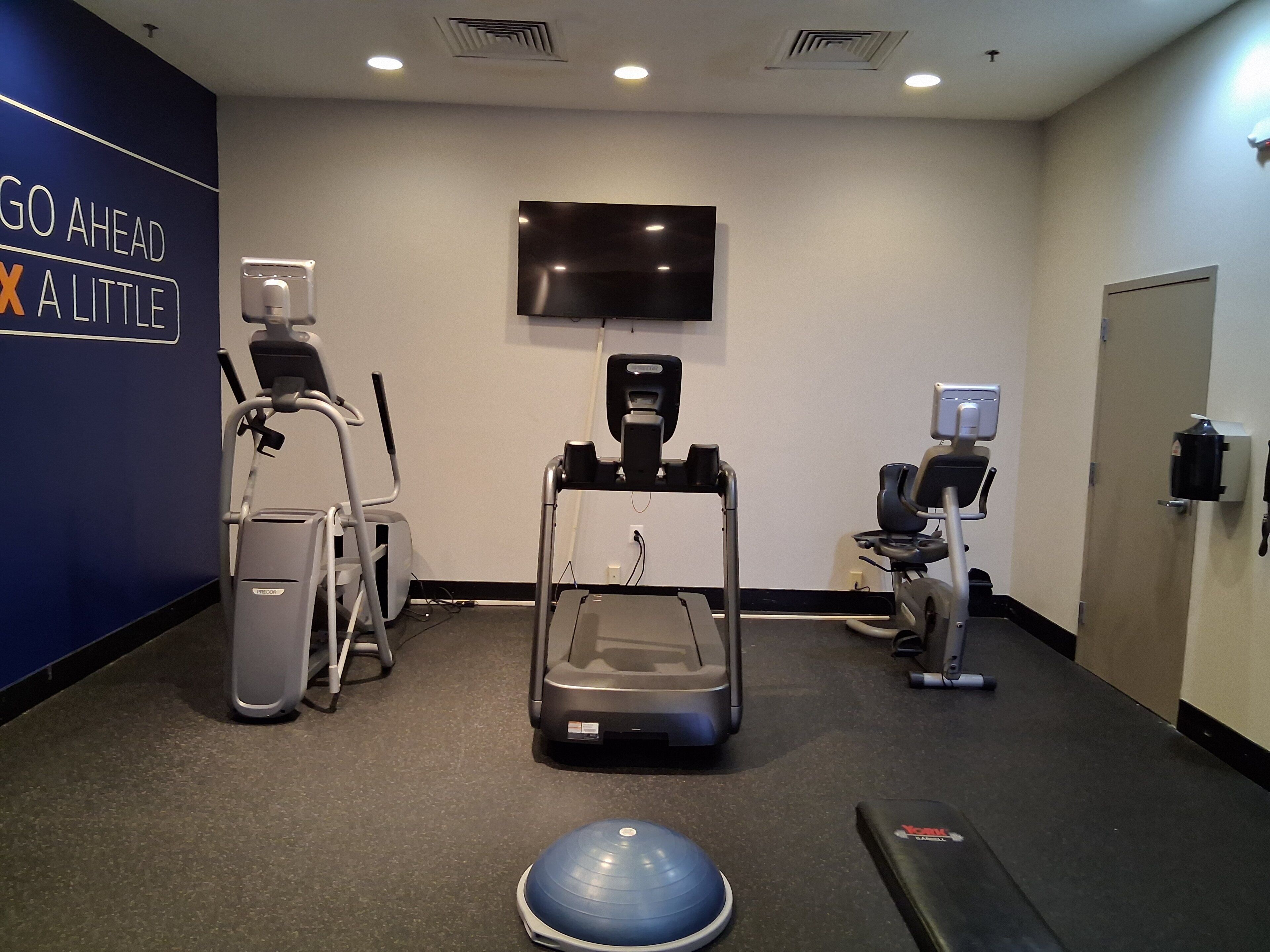 A gym with exercise equipment, a wall-mounted TV, and a motivational sign.