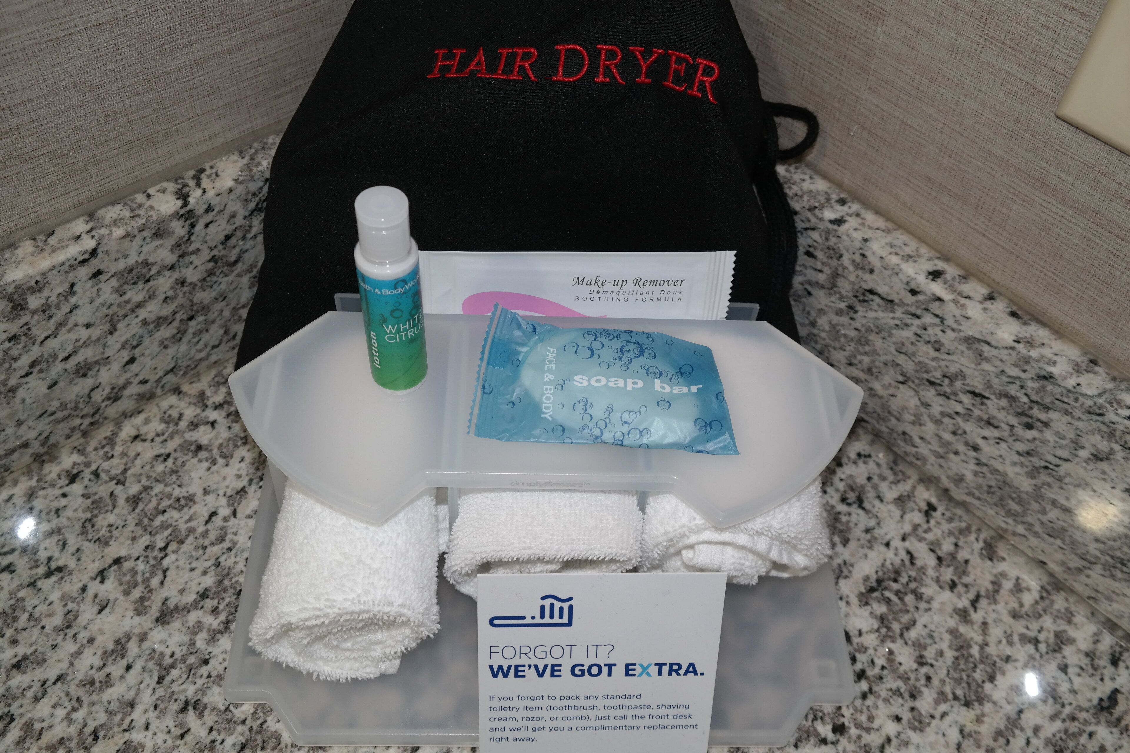 Habitación de hotel con secador de pelo, una botella de loción, jabón en barra y un cartel de oferta de reemplazo gratuito.