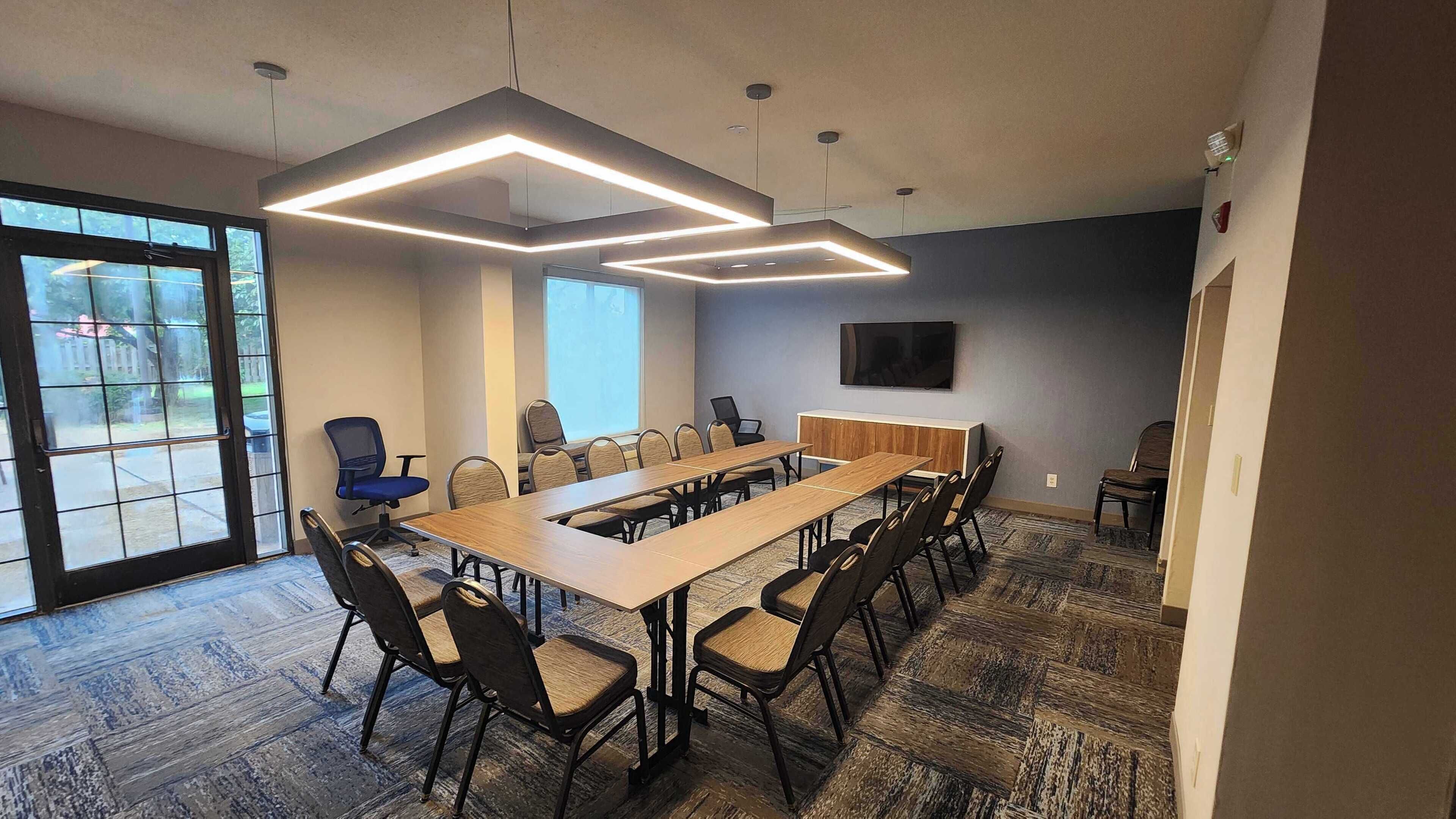 A conference room with a long table, multiple chairs, a television, and a large window.