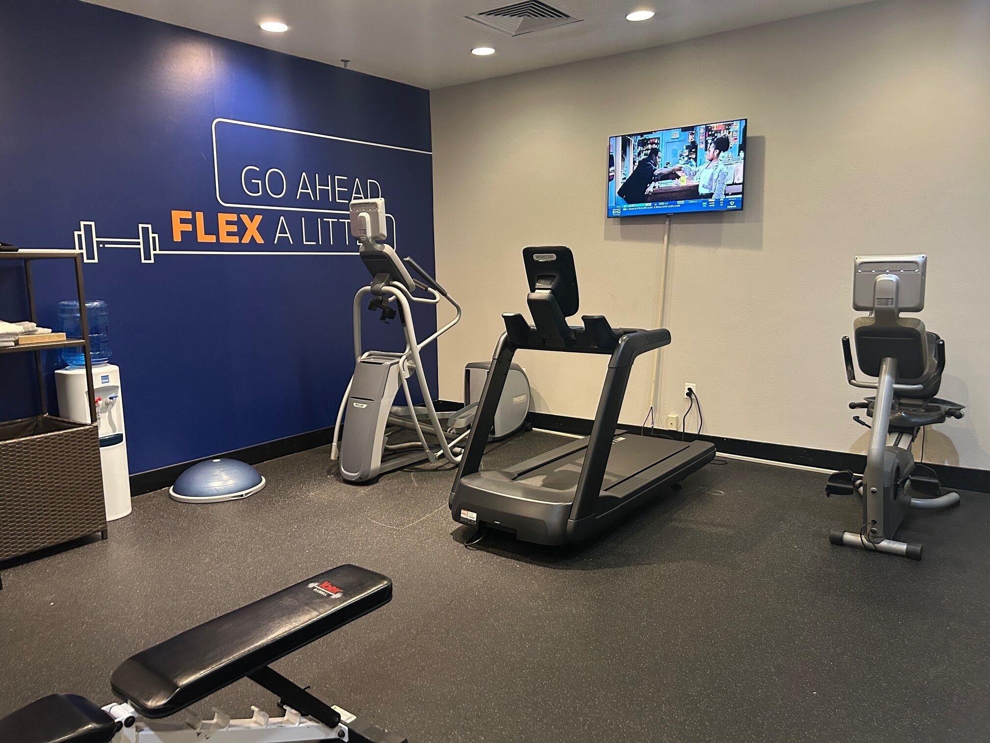 A gym with exercise equipment, a water dispenser, and a motivational wall sign.