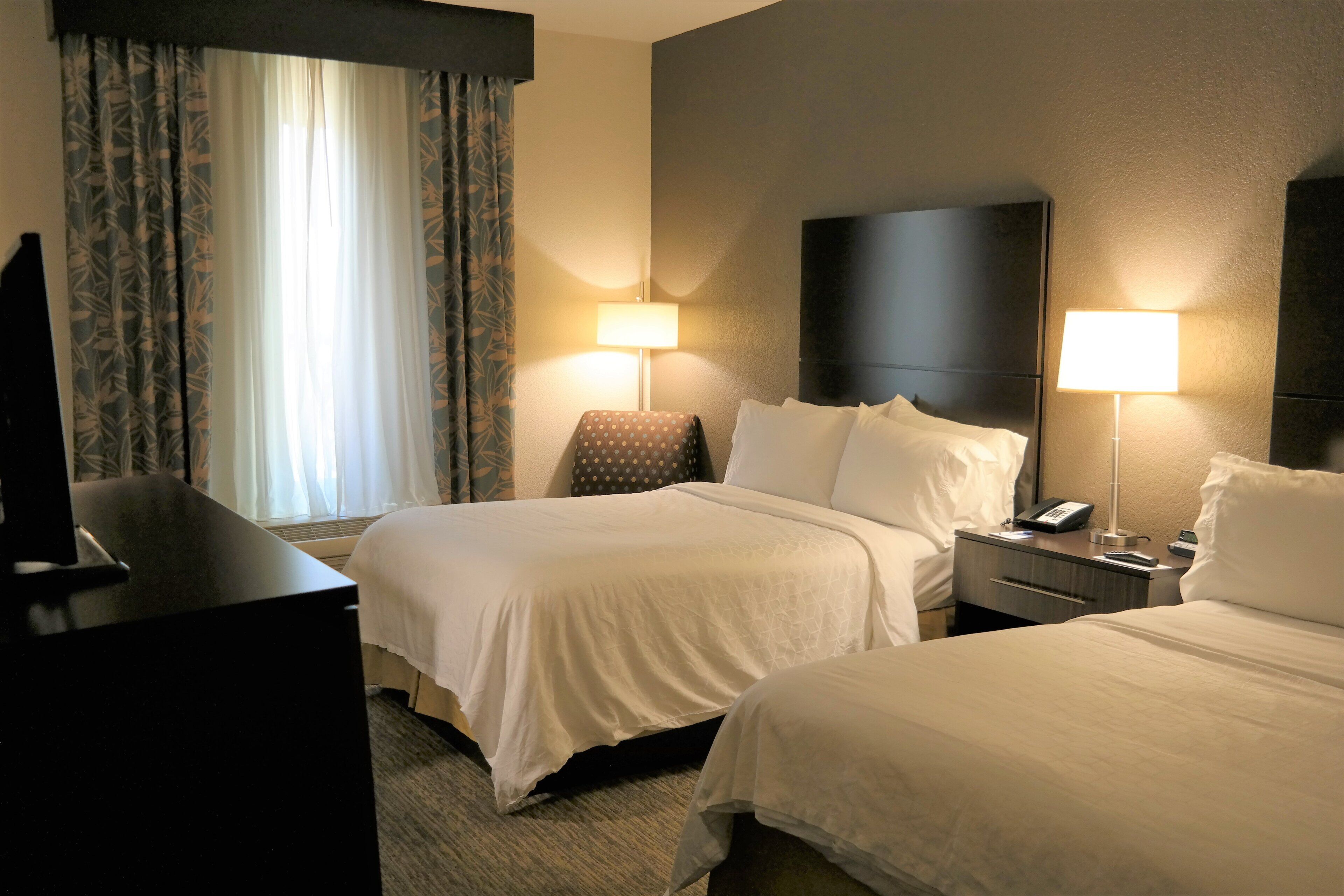 A hotel room with two beds, a desk, a chair, and a TV.